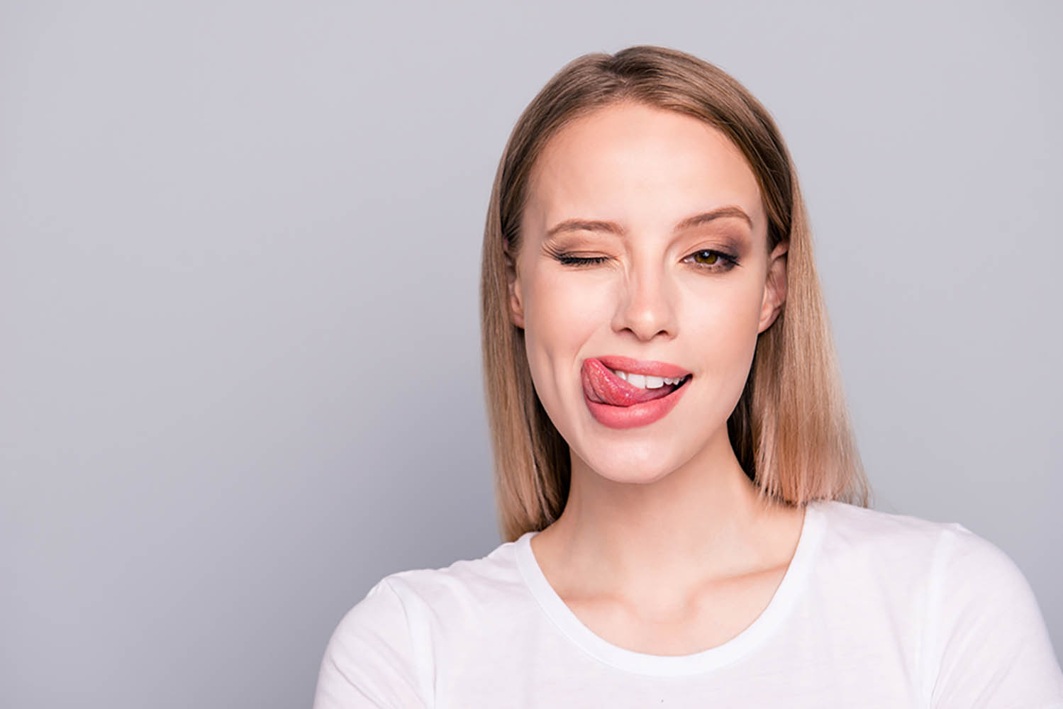 Close Up Portrait Of Playful And Sweet Girl Showing Tongue Giving Wink Isolated Gray Background With Copy Space For Text